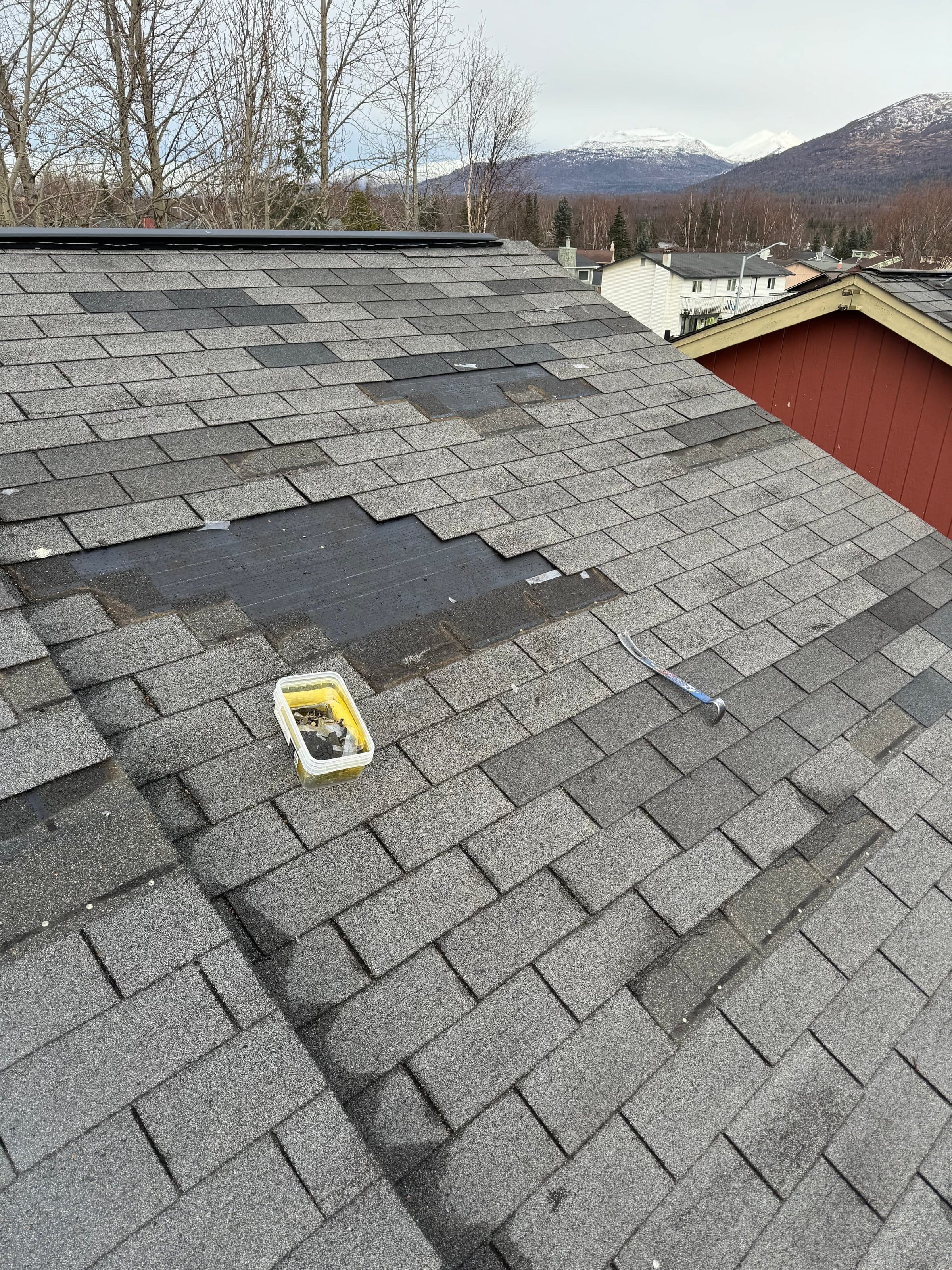 Black Spruce Roofing documenting wind damage on an Anchorage roof, Chugach Mountains in the background